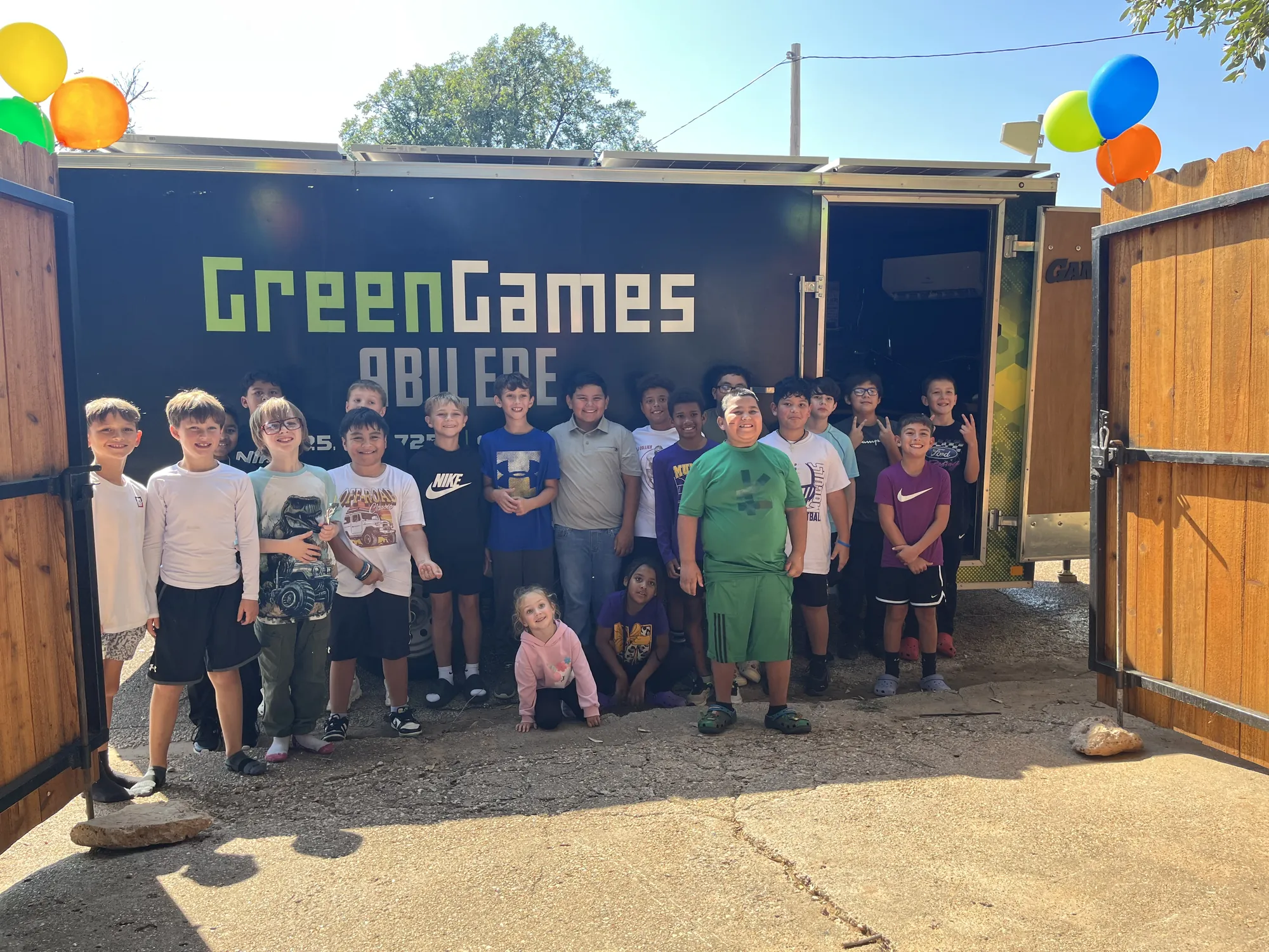 Birthday party guests posing with balloons in front of the game trailer in a backyard