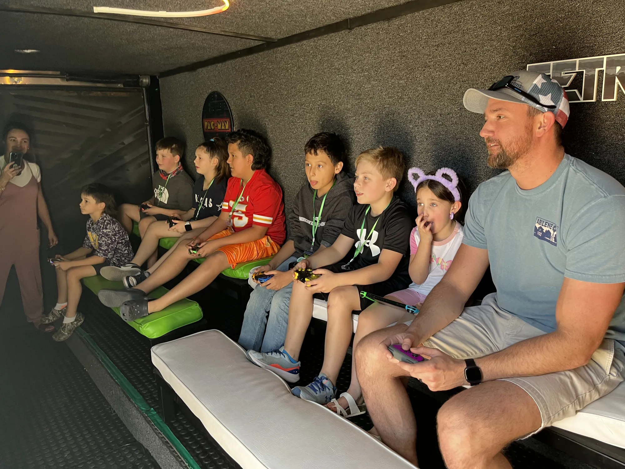 A dad playing video games on the bench with a row of kids at a birthday party