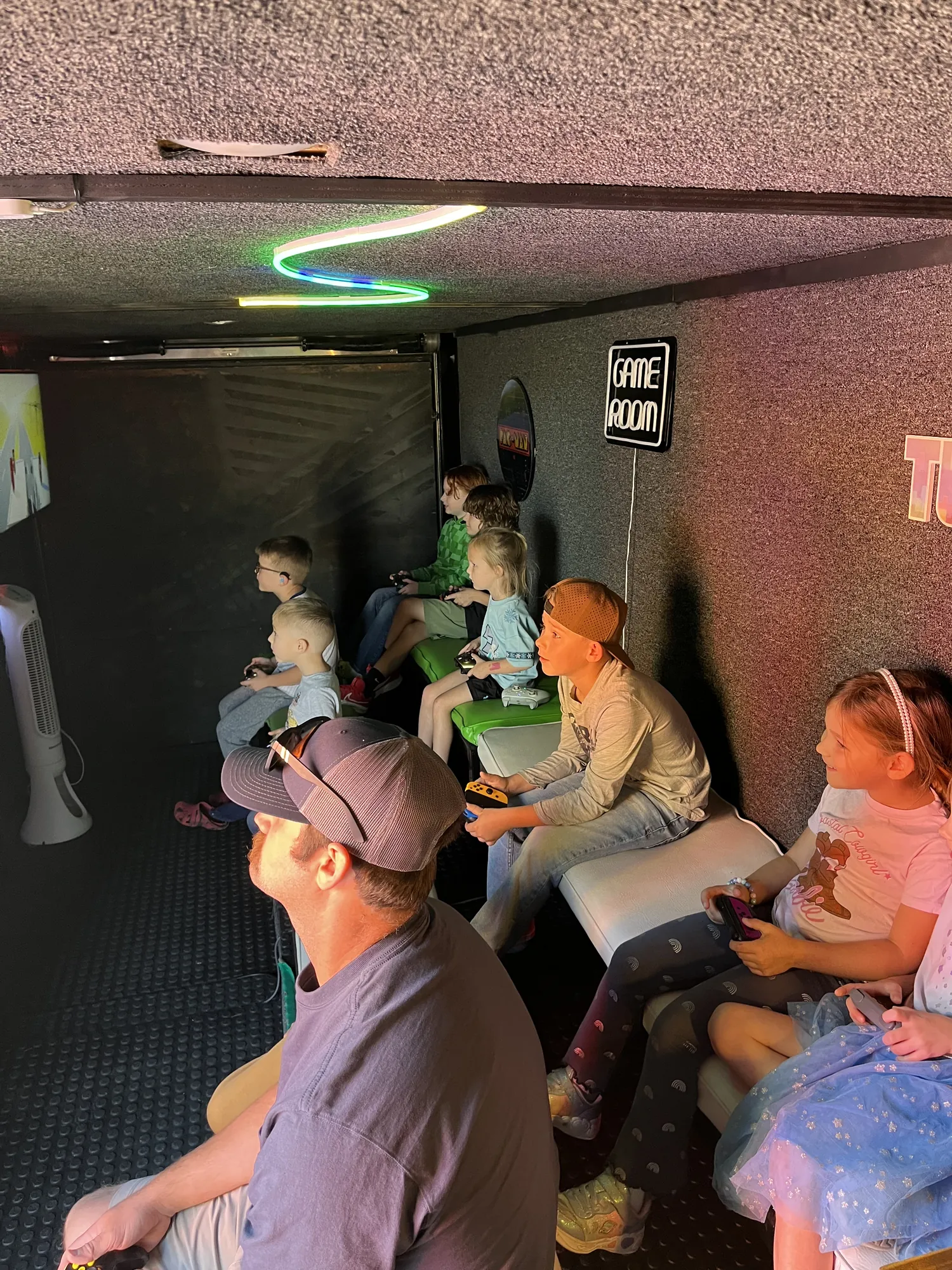 Kids and a grown-up on the benches inside the trailer under neon lights