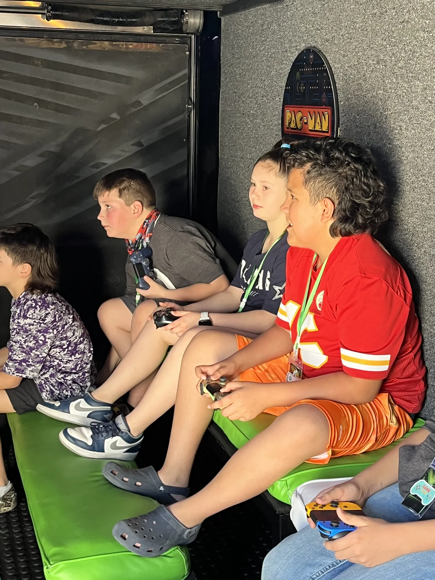 Kids in team jerseys holding controllers on the green benches