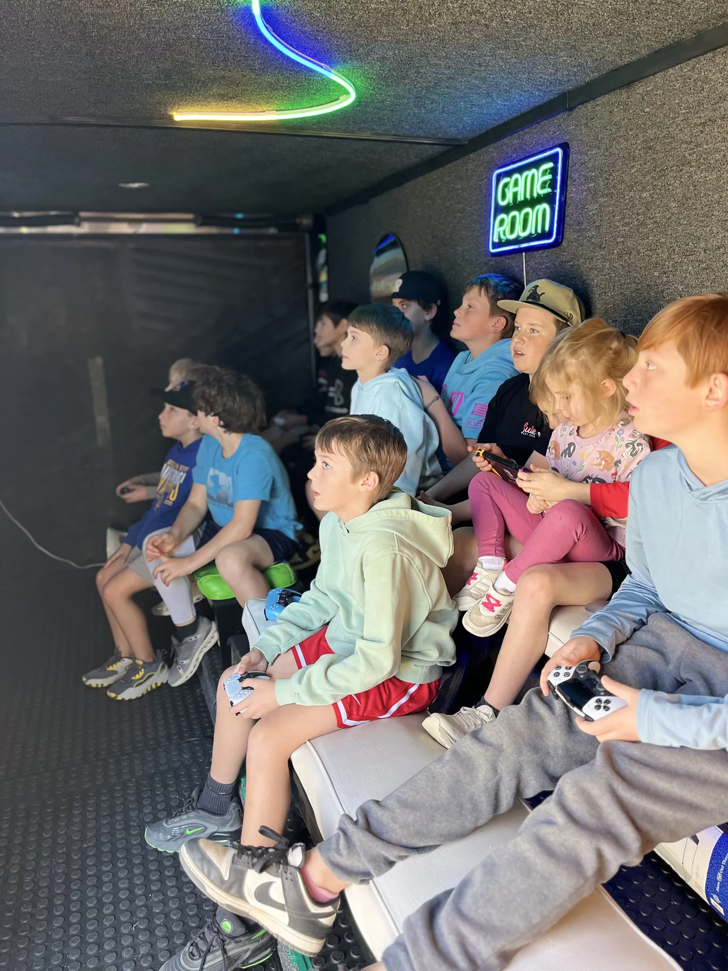 A trailer full of kids and teens playing video games under the neon Game Room sign