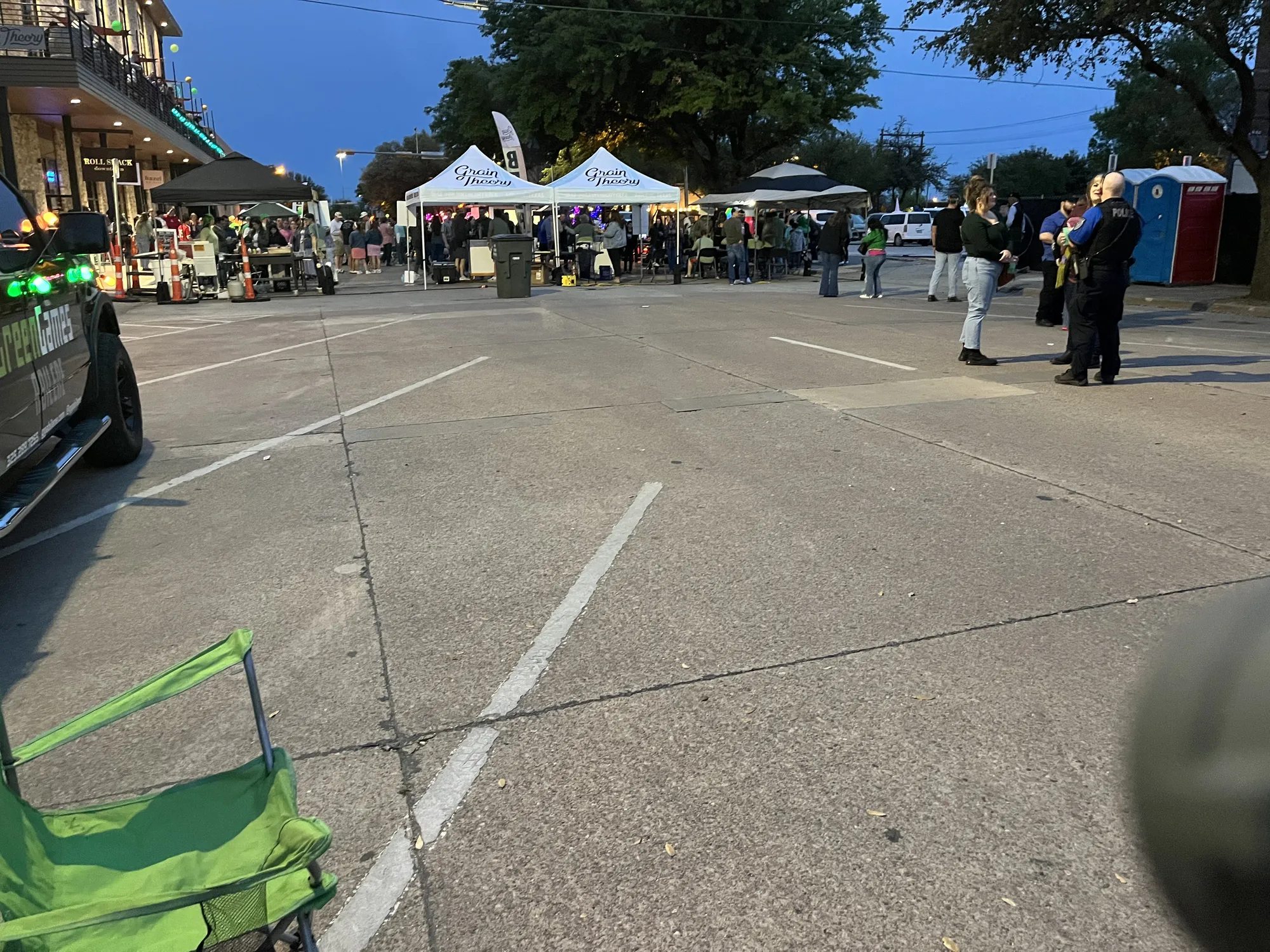 Grain Theory’s white tents lit up along a downtown Abilene street at dusk, with the Green Games truck parked at the edge