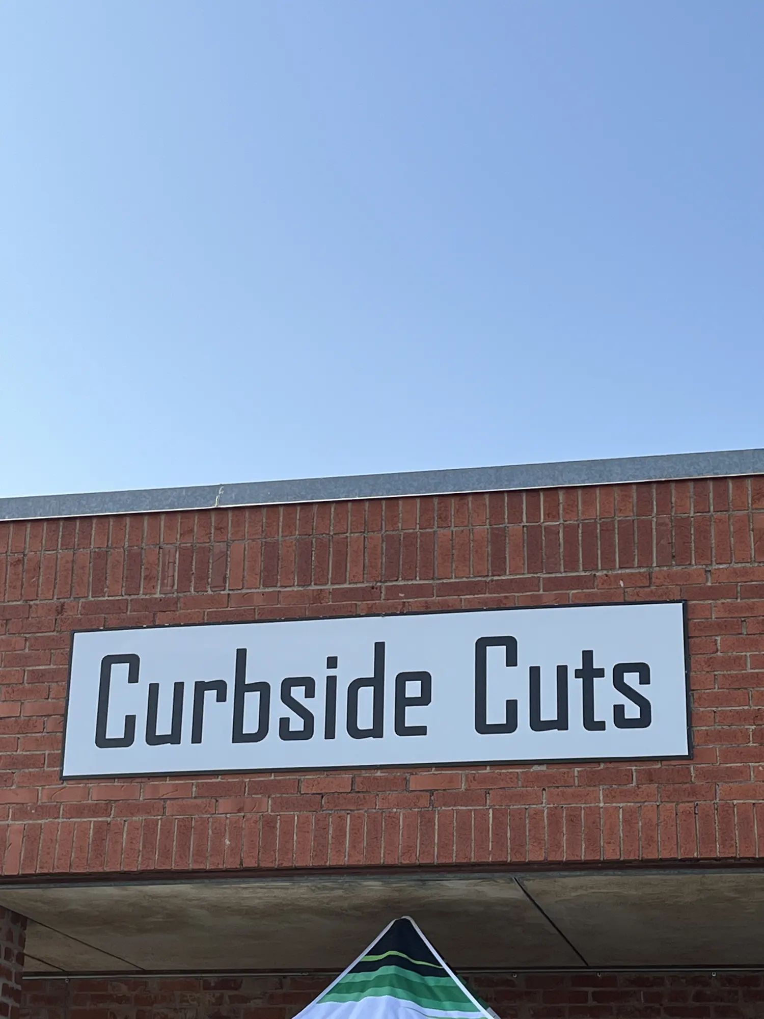 The Curbside Cuts sign on a brick storefront in Abilene, with a shade tent below