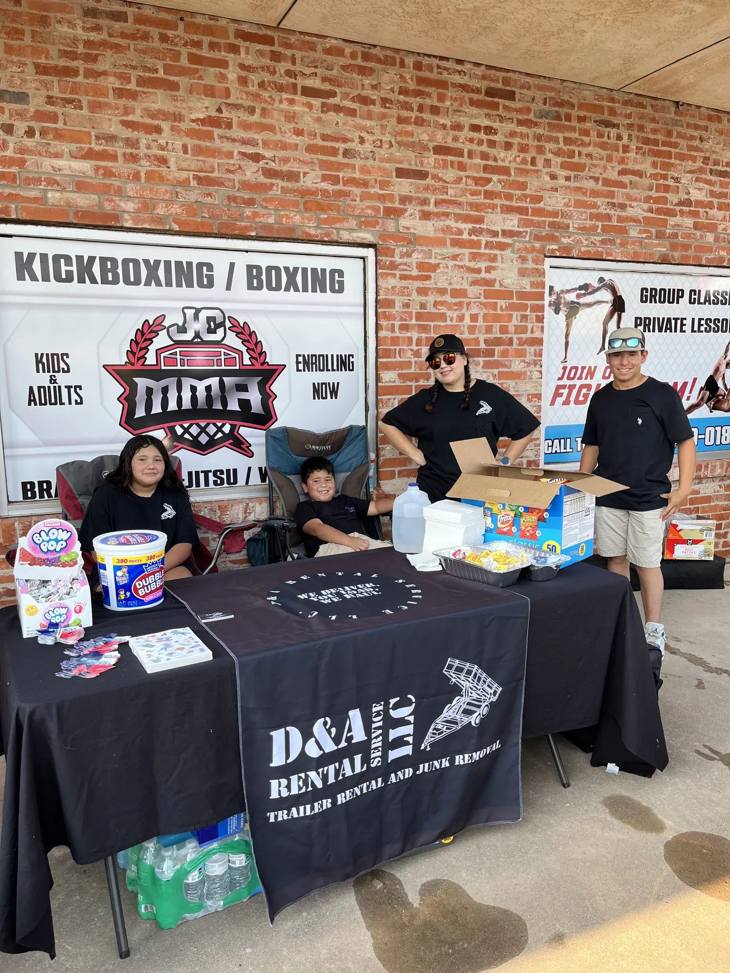 Volunteers at a sponsor table with snacks and candy outside Curbside Cuts on back-to-school day
