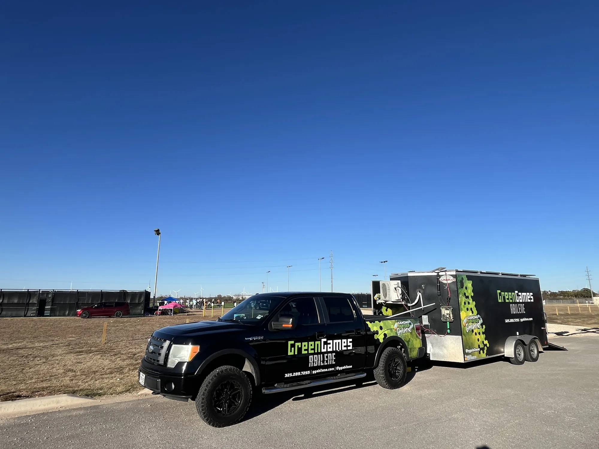 The Green Games truck and trailer parked by the football field under a clear blue sky