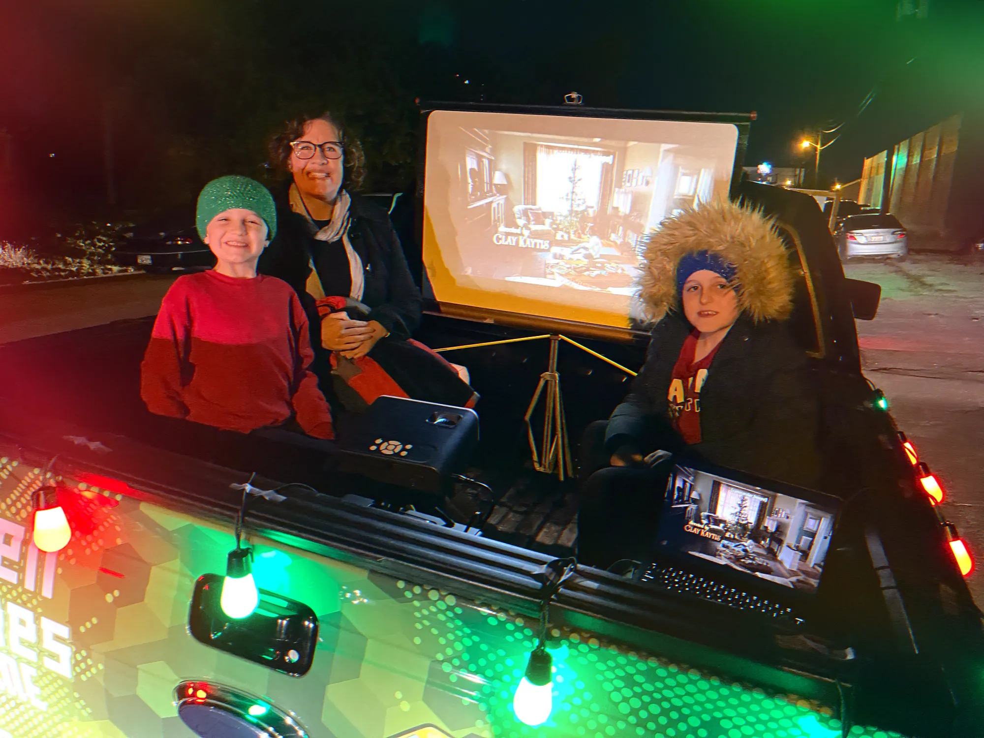 Kids in winter hats playing a video game in the lit-up bed of the Green Games truck