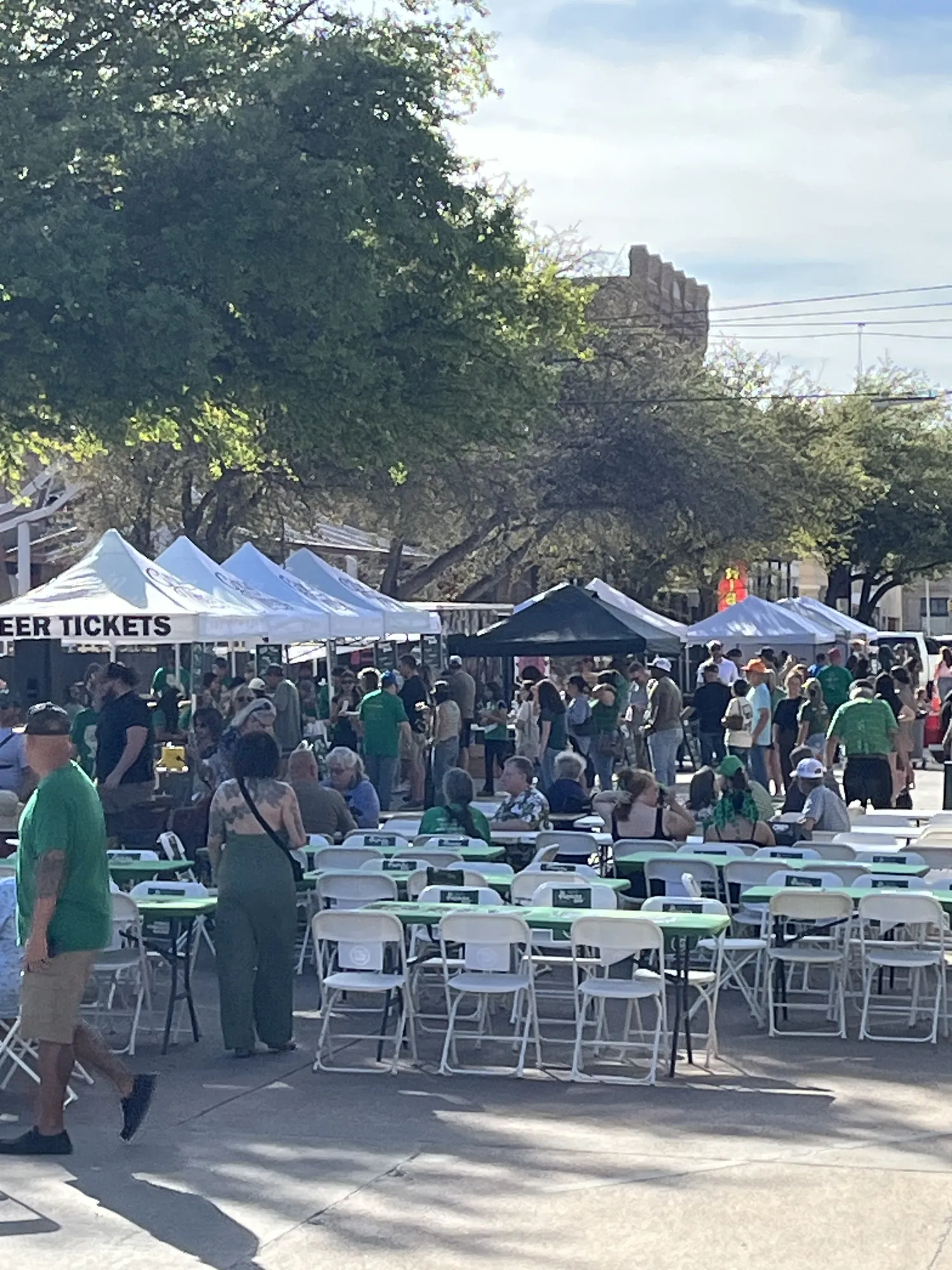A crowd dressed in green at long tables during a St. Patrick’s Day street party in downtown Abilene