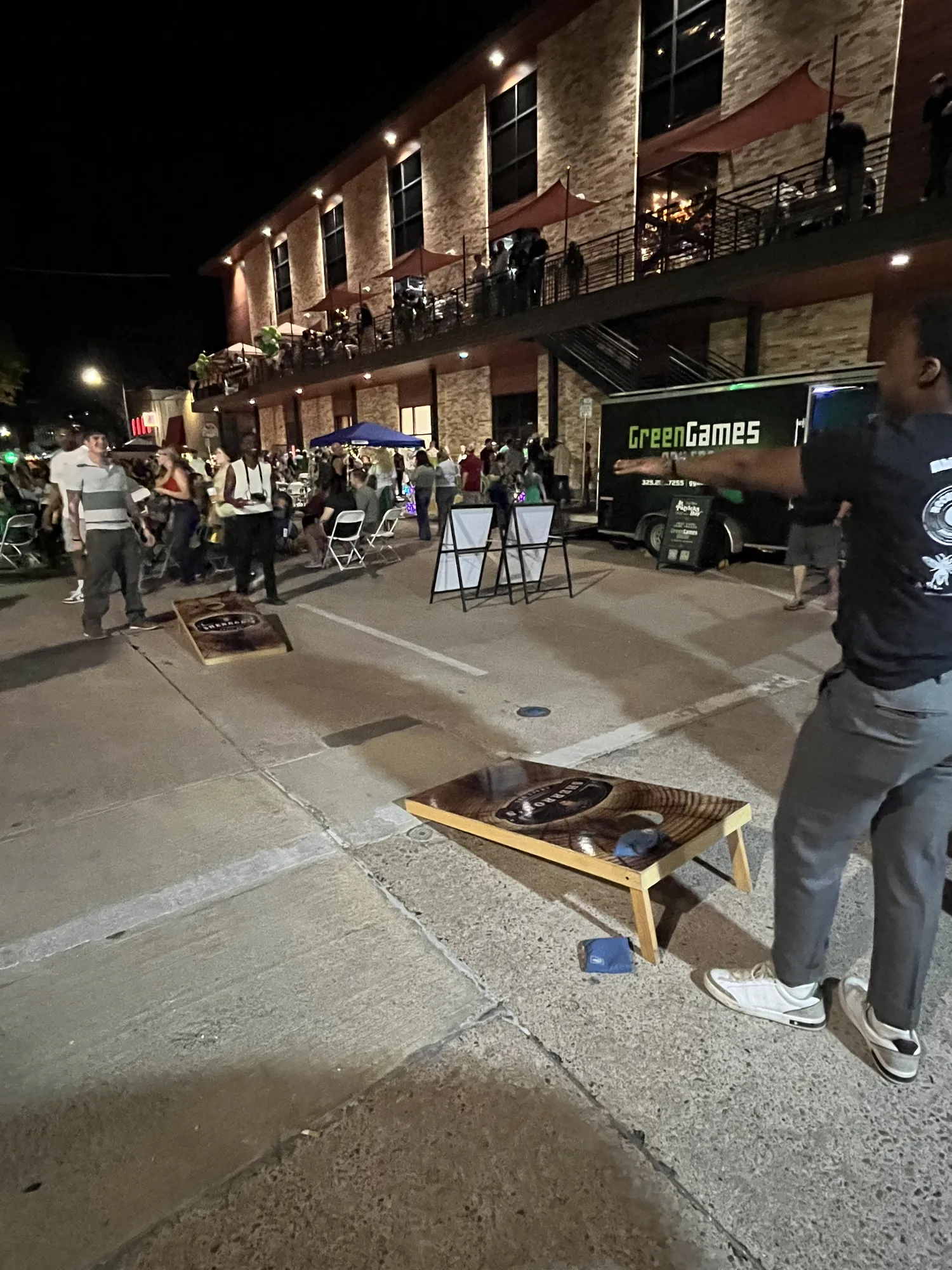 The Green Games truck parked on a downtown Abilene street at night beside cornhole boards