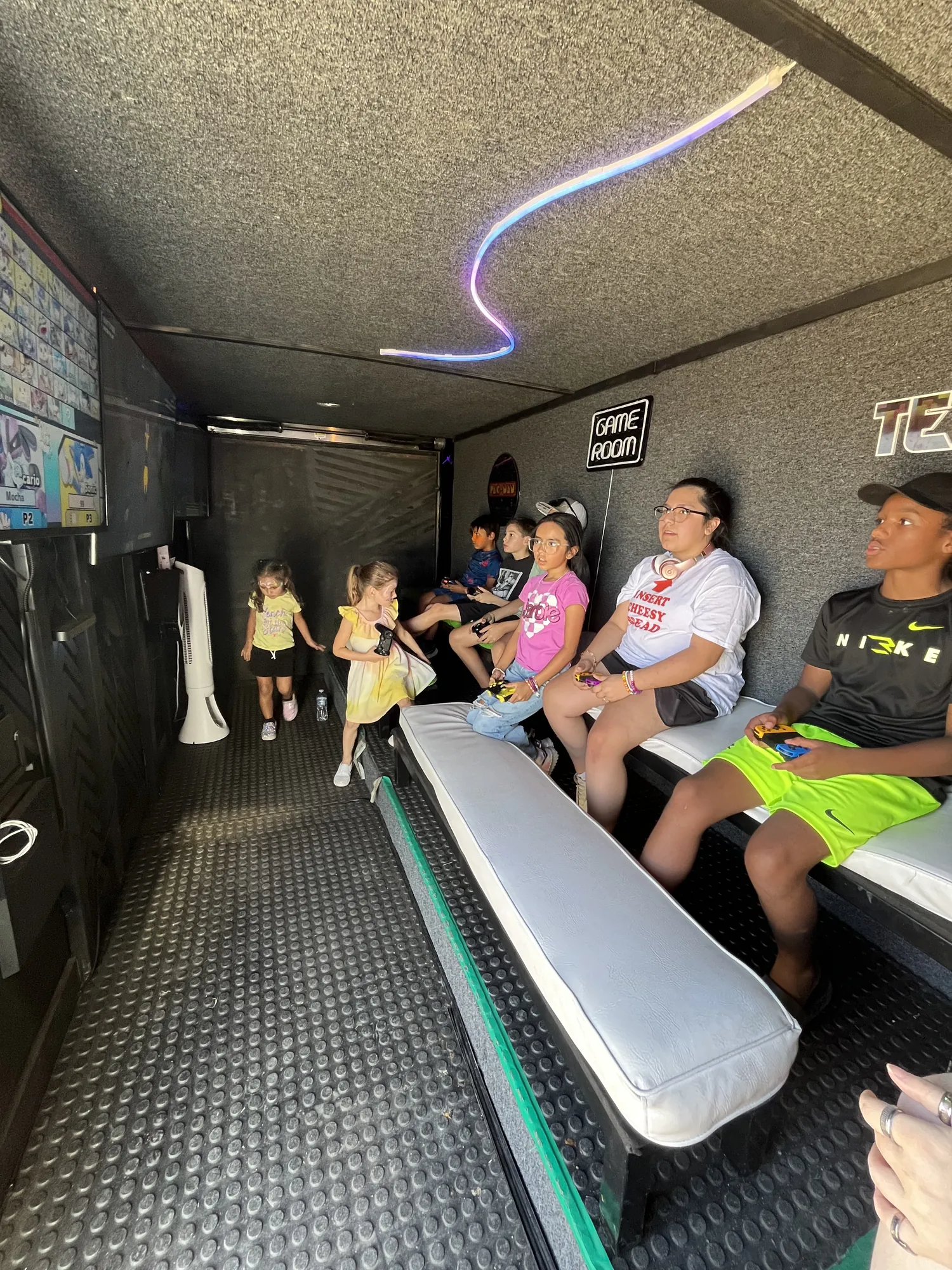Kids and a parent playing video games on the benches inside the Green Games trailer