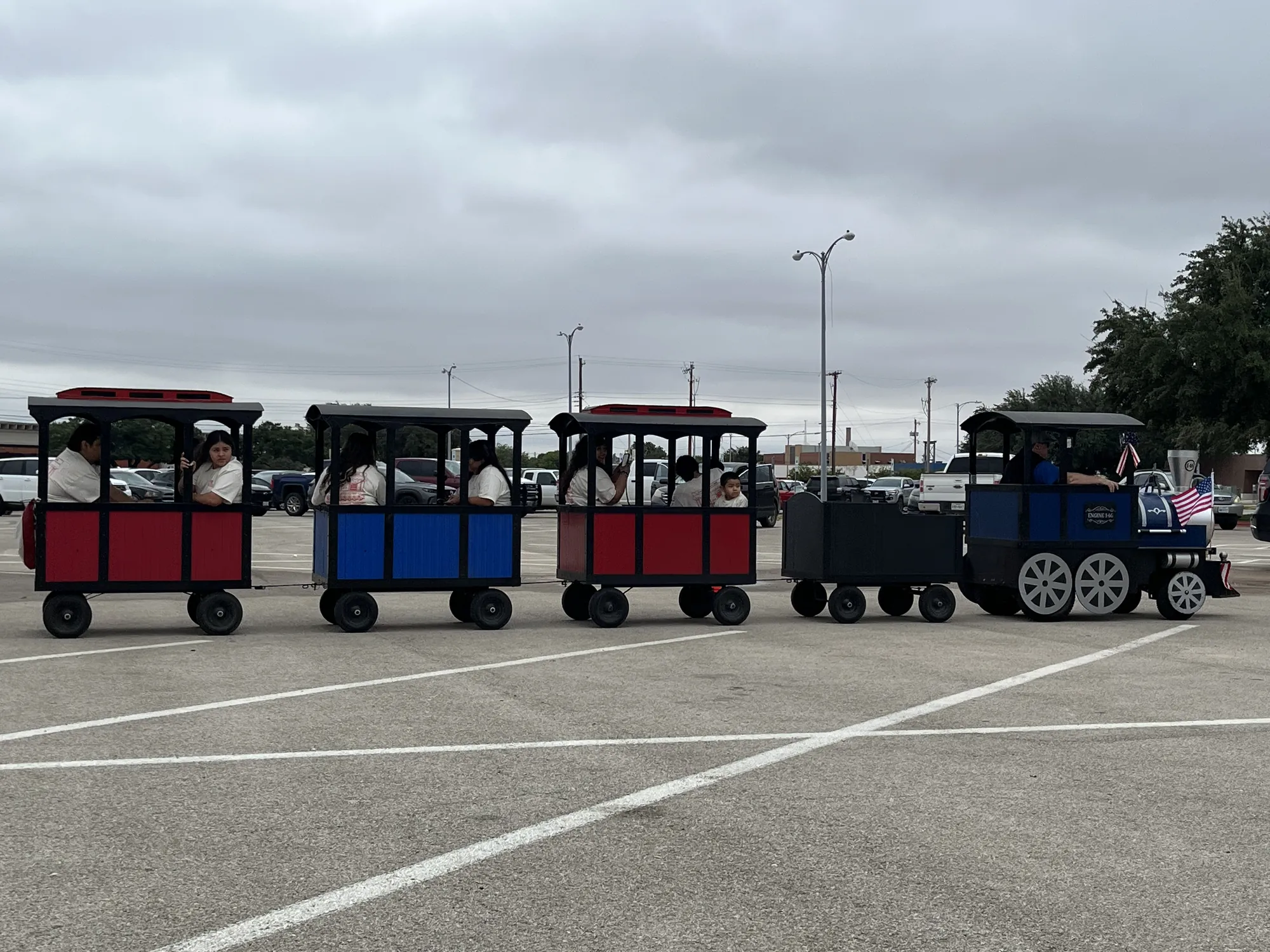 Families riding a colorful trackless train around the parking lot at a company picnic