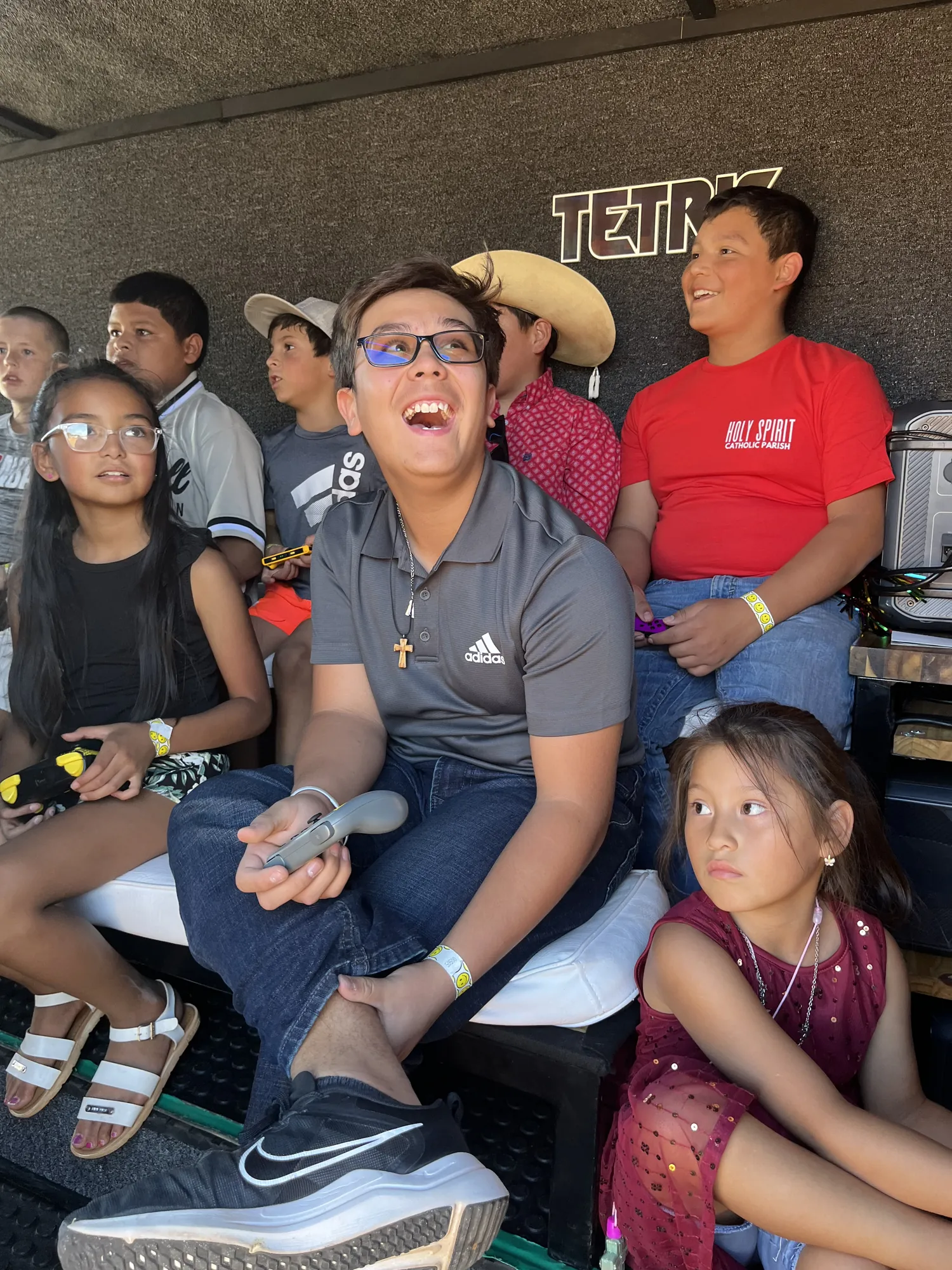 A teen laughing with a controller in hand while friends play beside him in the trailer