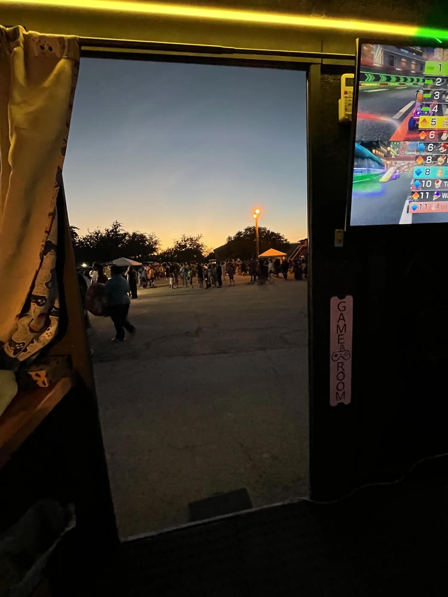 The view out the trailer door at dusk, with festival booths and families across the lot