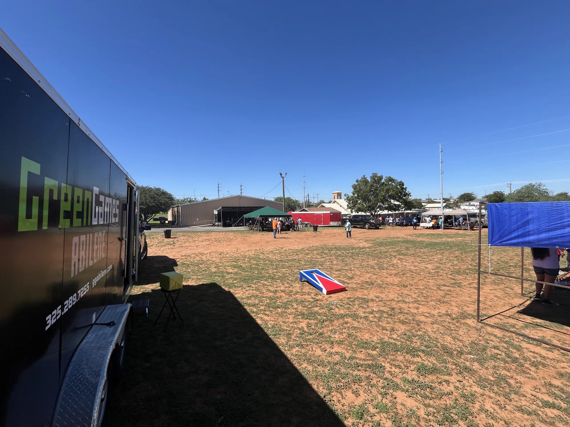 The Green Games trailer beside a field of fall festival games and cornhole boards under a blue sky