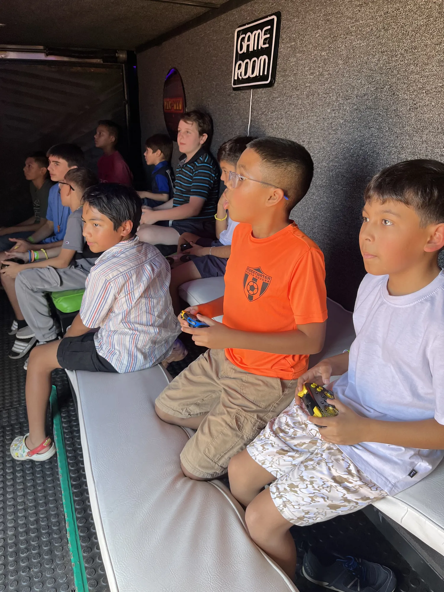 Boys on the trailer benches staring up at the big screens under the Game Room sign