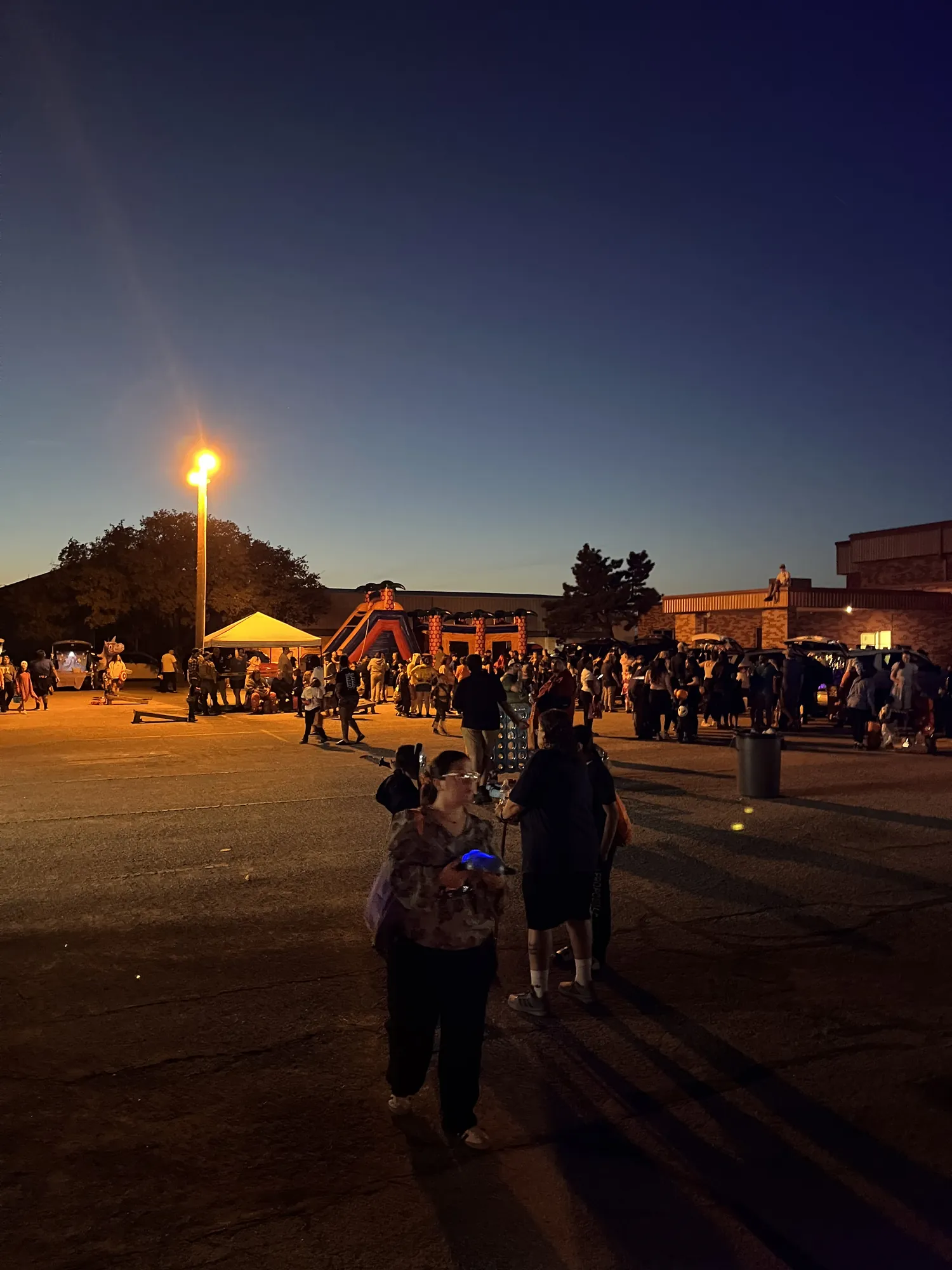 Families walking between booths under the lights after dark at a church fall festival