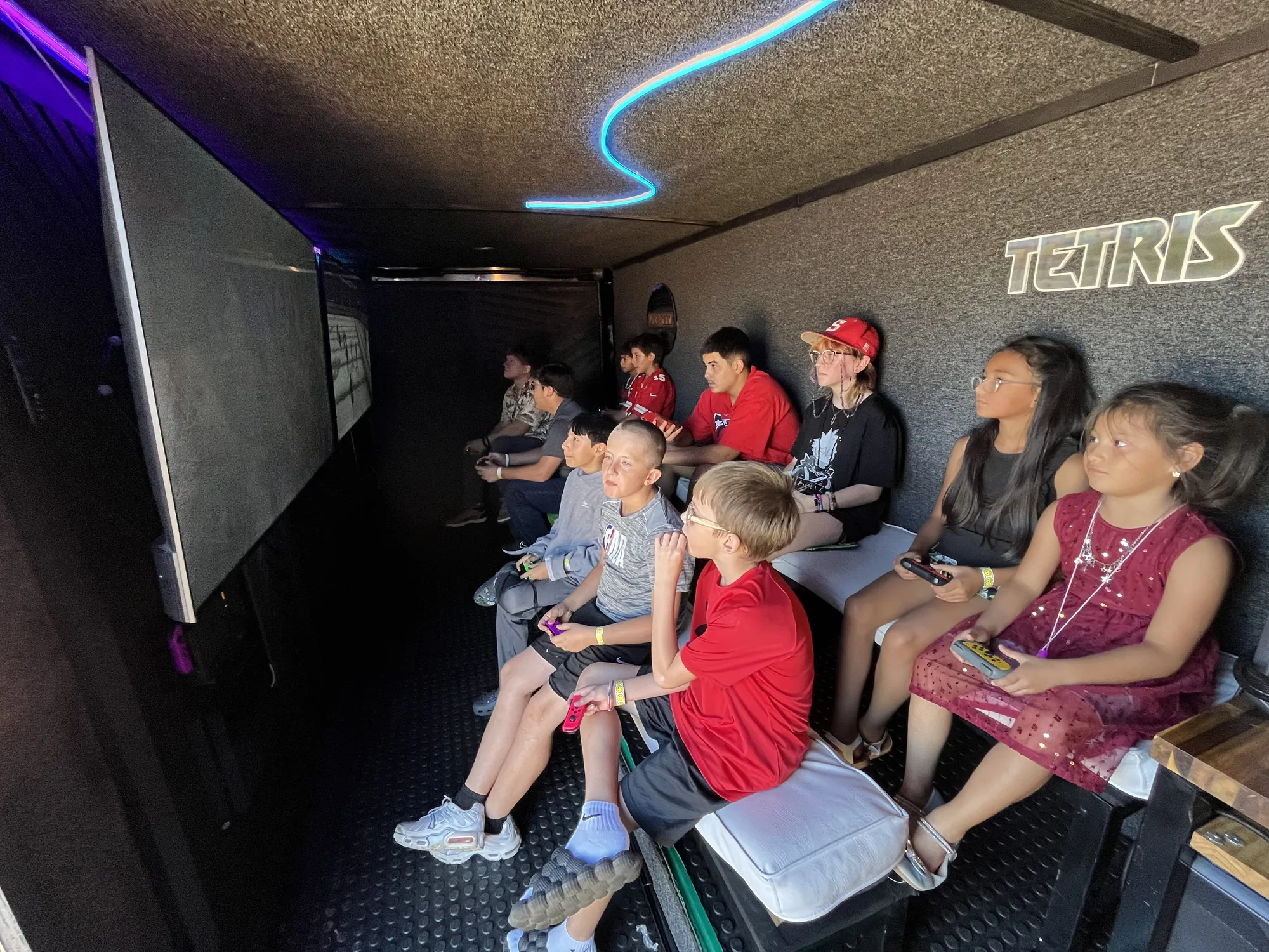 Kids lined up on the benches playing video games inside the trailer at a fall festival