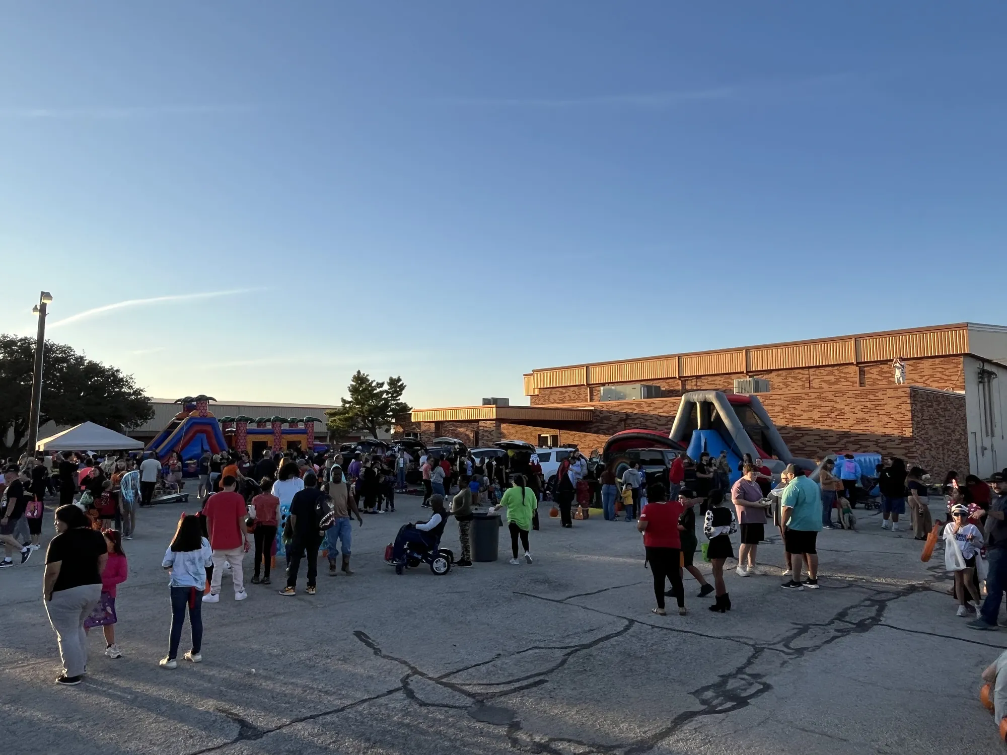 A big crowd filling the parking lot at sunset during a church fall festival, with the inflatables and the trailer beyond