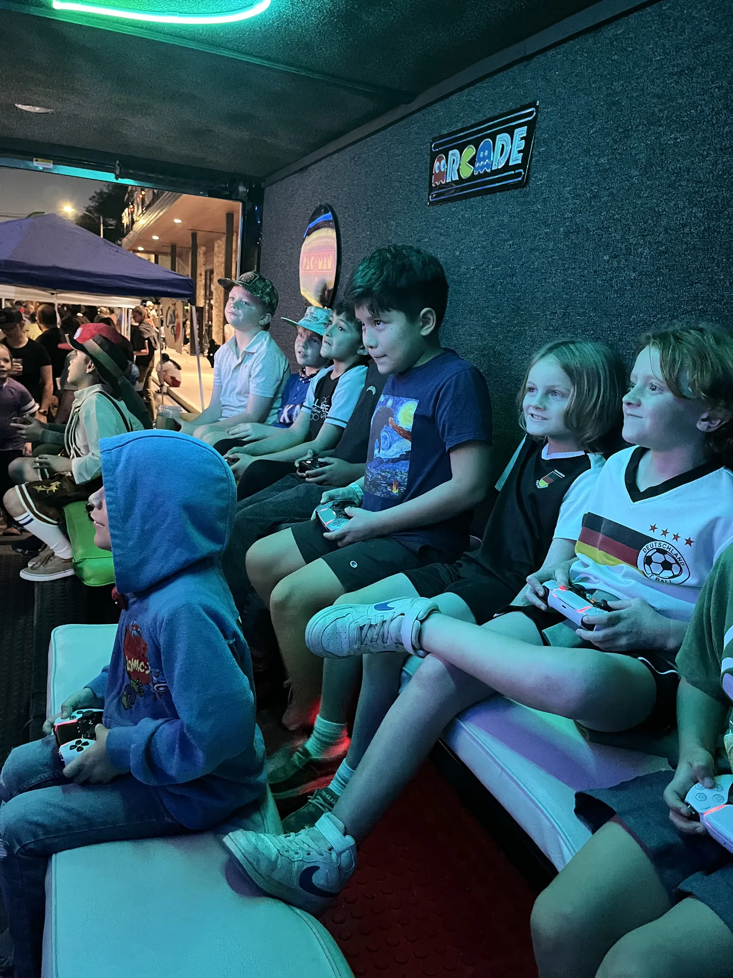 A row of kids playing video games under the trailer’s colorful lights