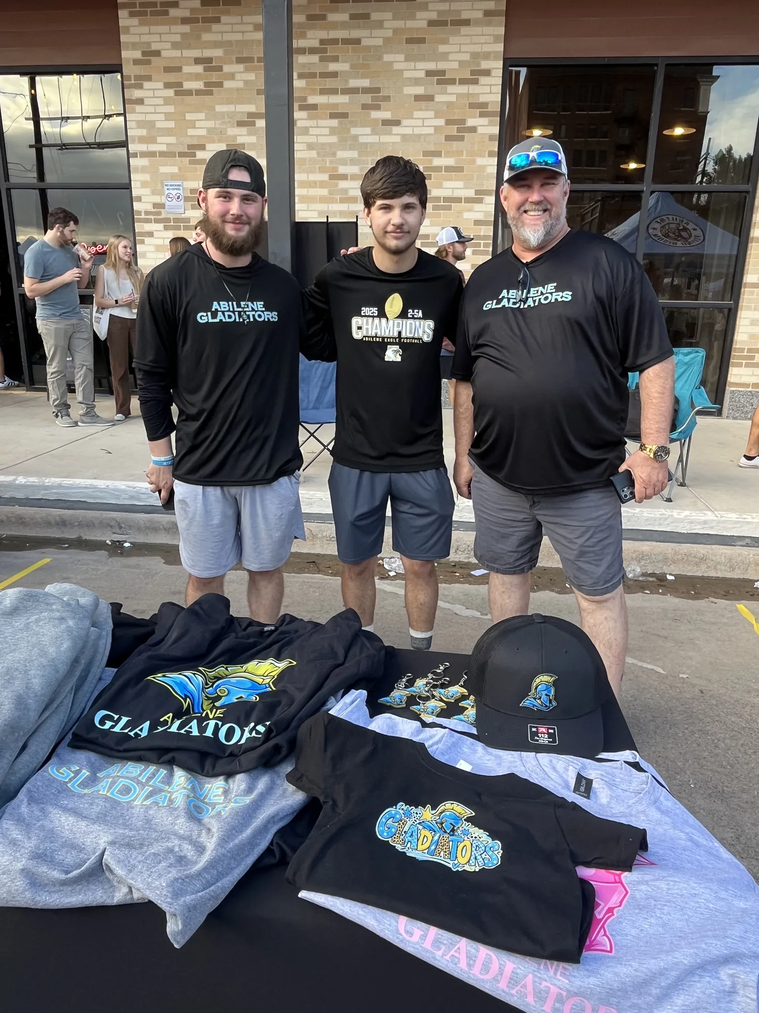 Three men from the Abilene Gladiators behind a table of team shirts and hats