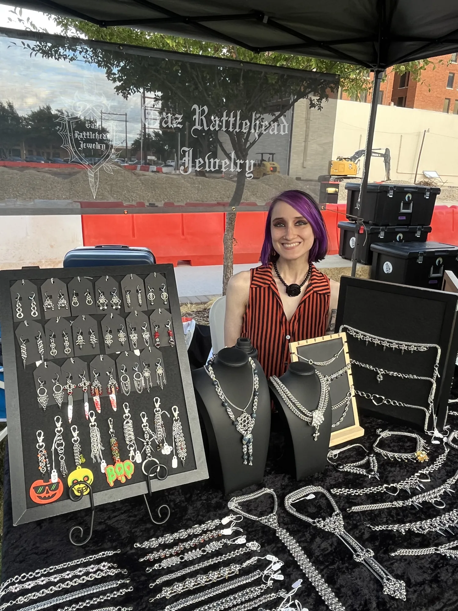A vendor at the Gaz Rattlehead Jewelry booth beside displays of handmade chain jewelry and earrings