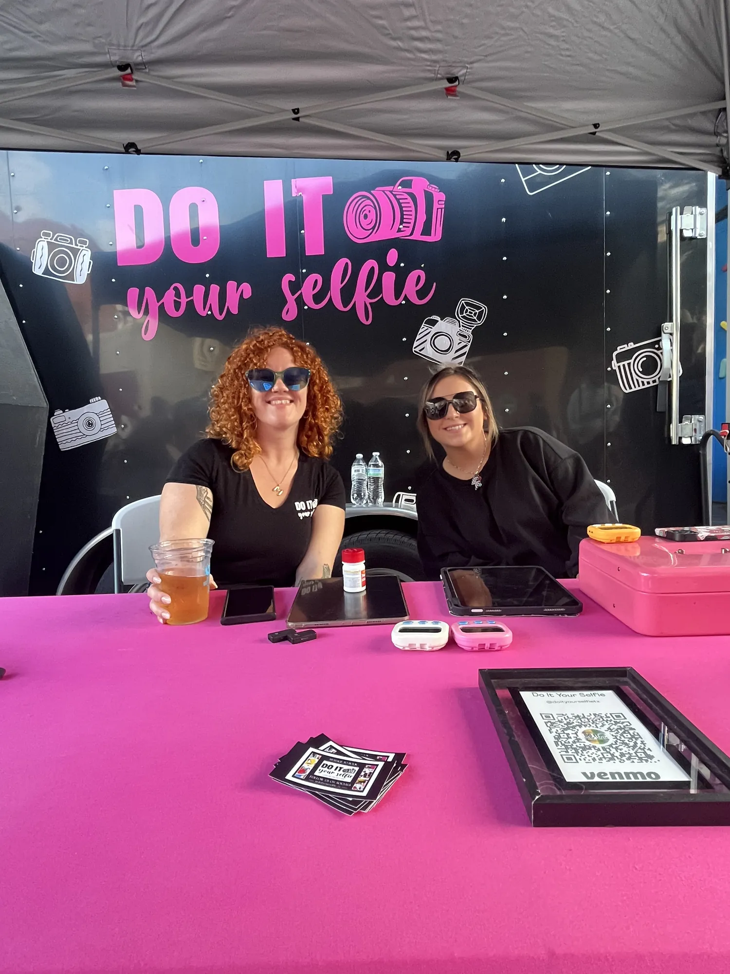 Two women at the bright pink Do It Your Selfie booth