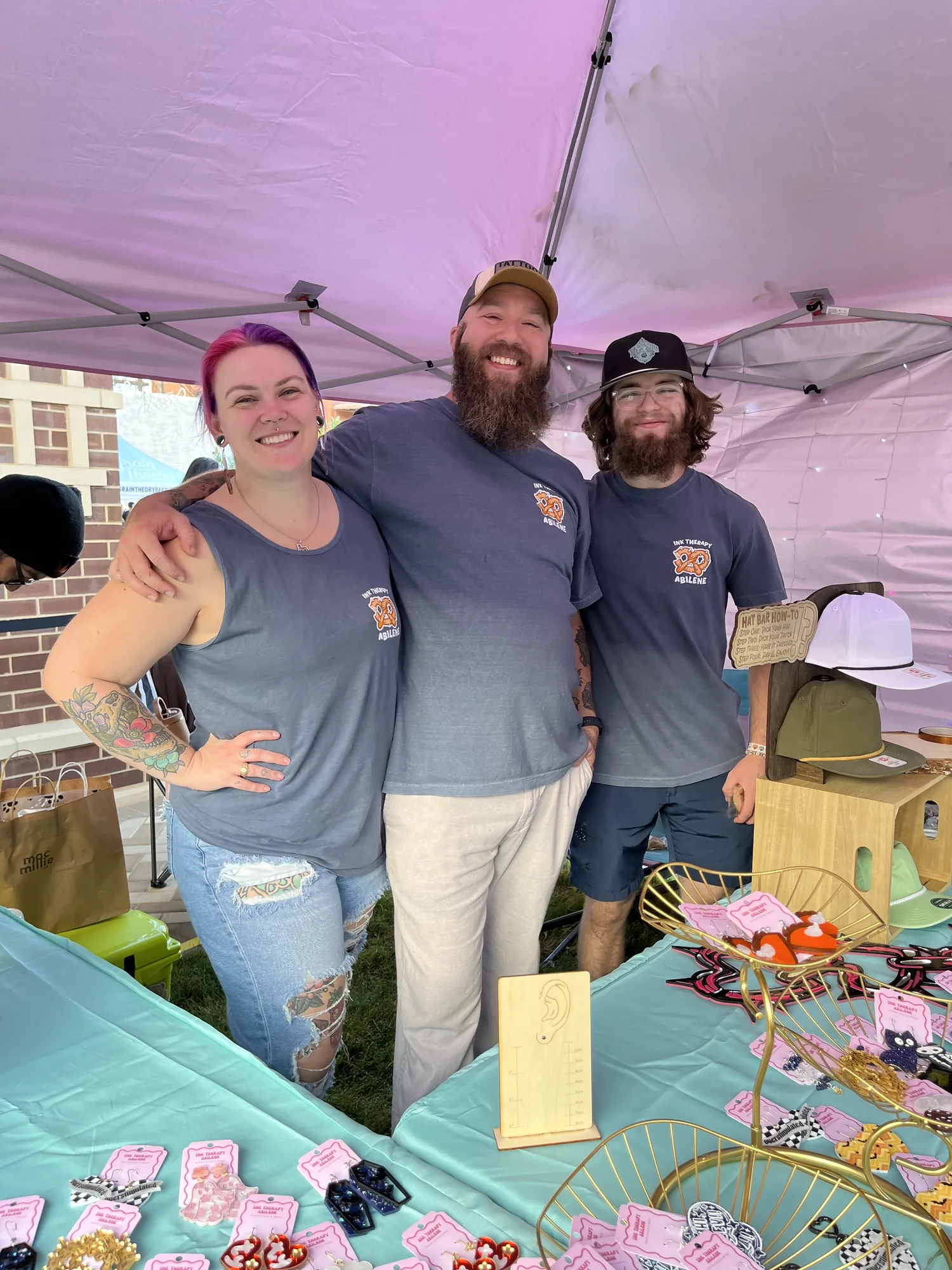 Three smiling vendors under a pink tent