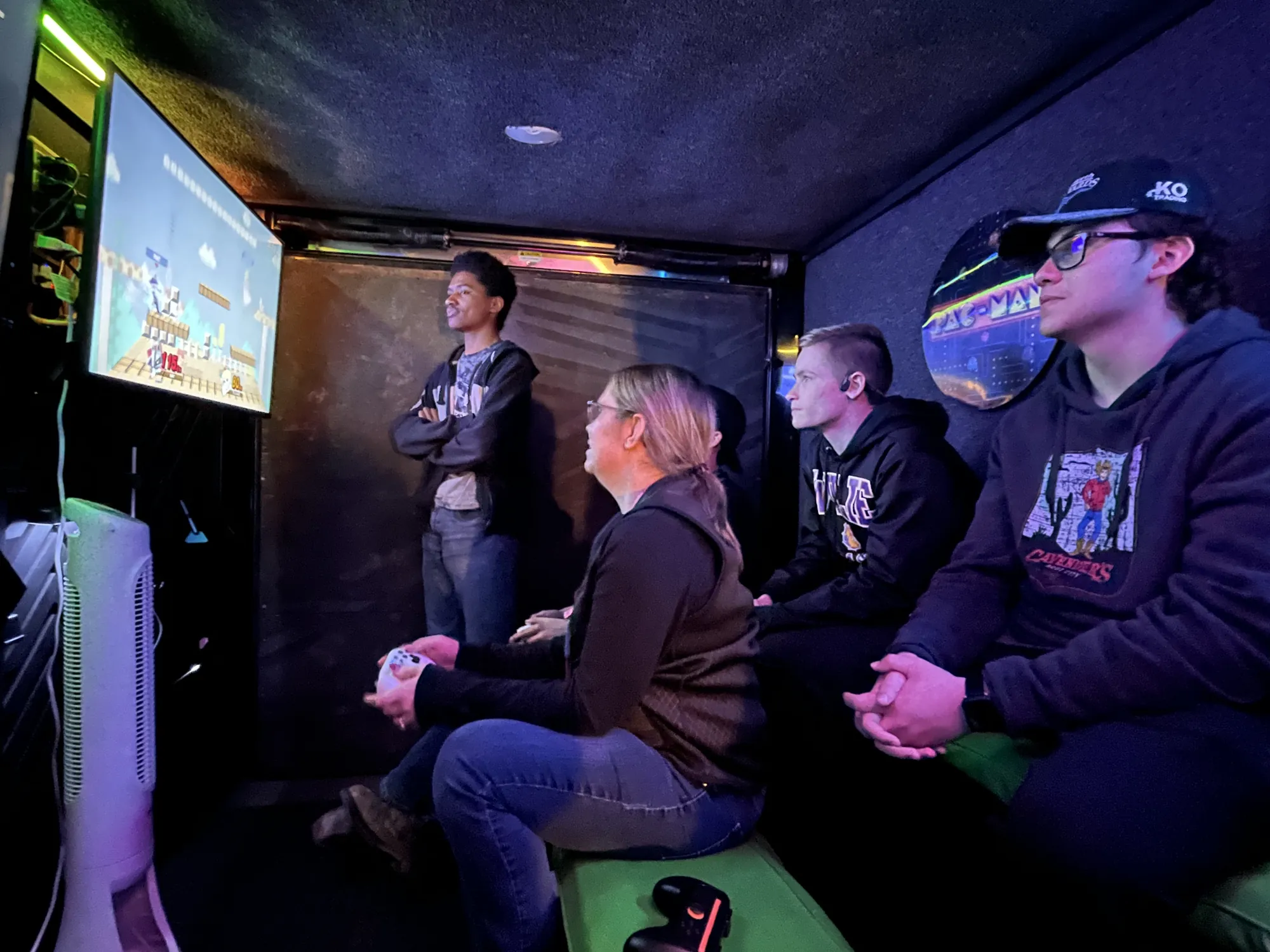 High school students and a chaperone playing a fighting game on the trailer’s big screen at a club night