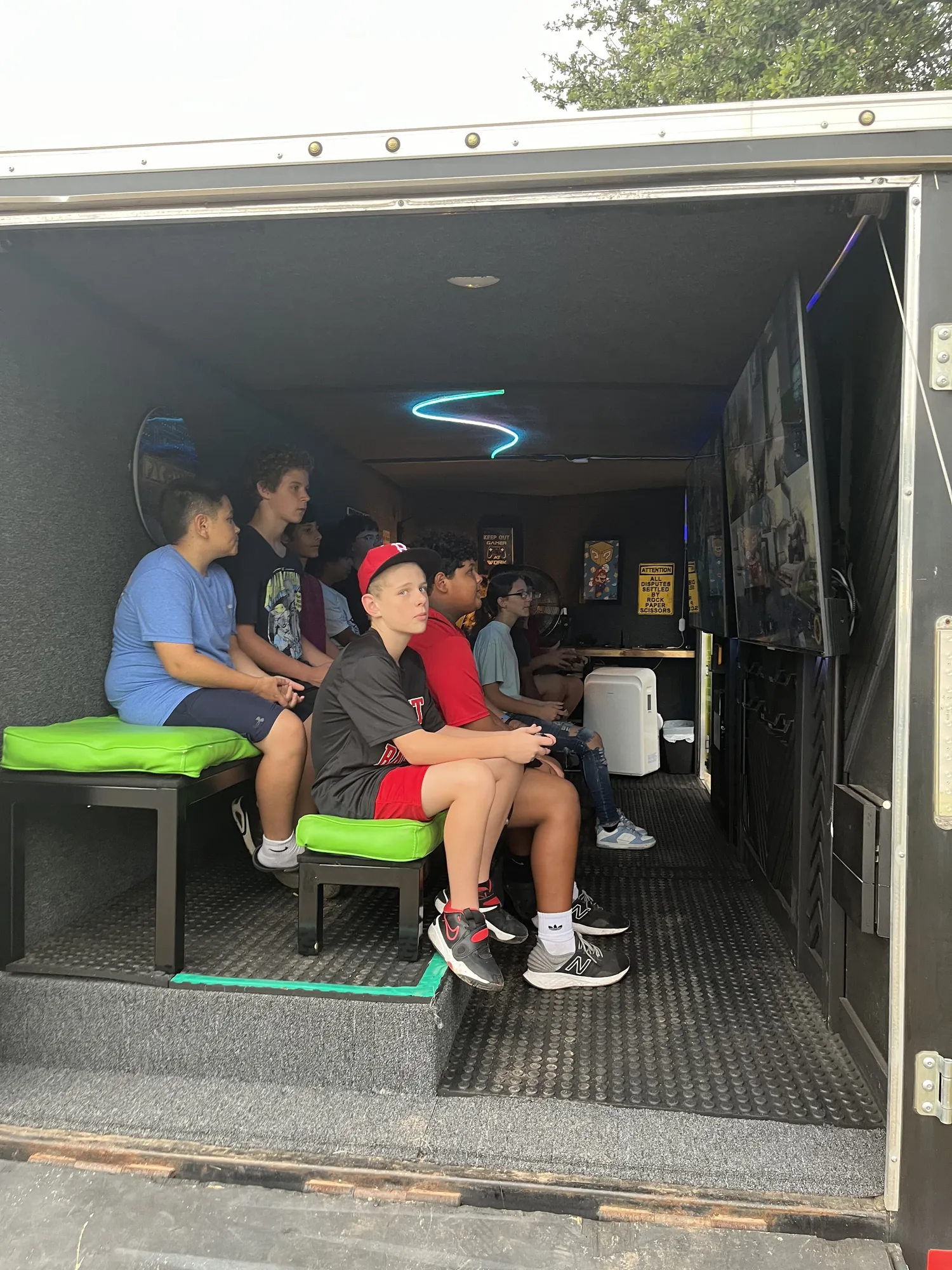 Students playing video games on the green benches inside the trailer during a school field day