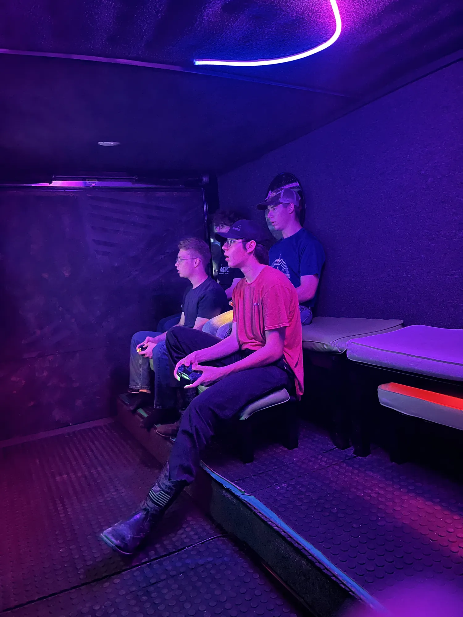 Recent graduates playing video games under purple lights inside the trailer at a graduation party