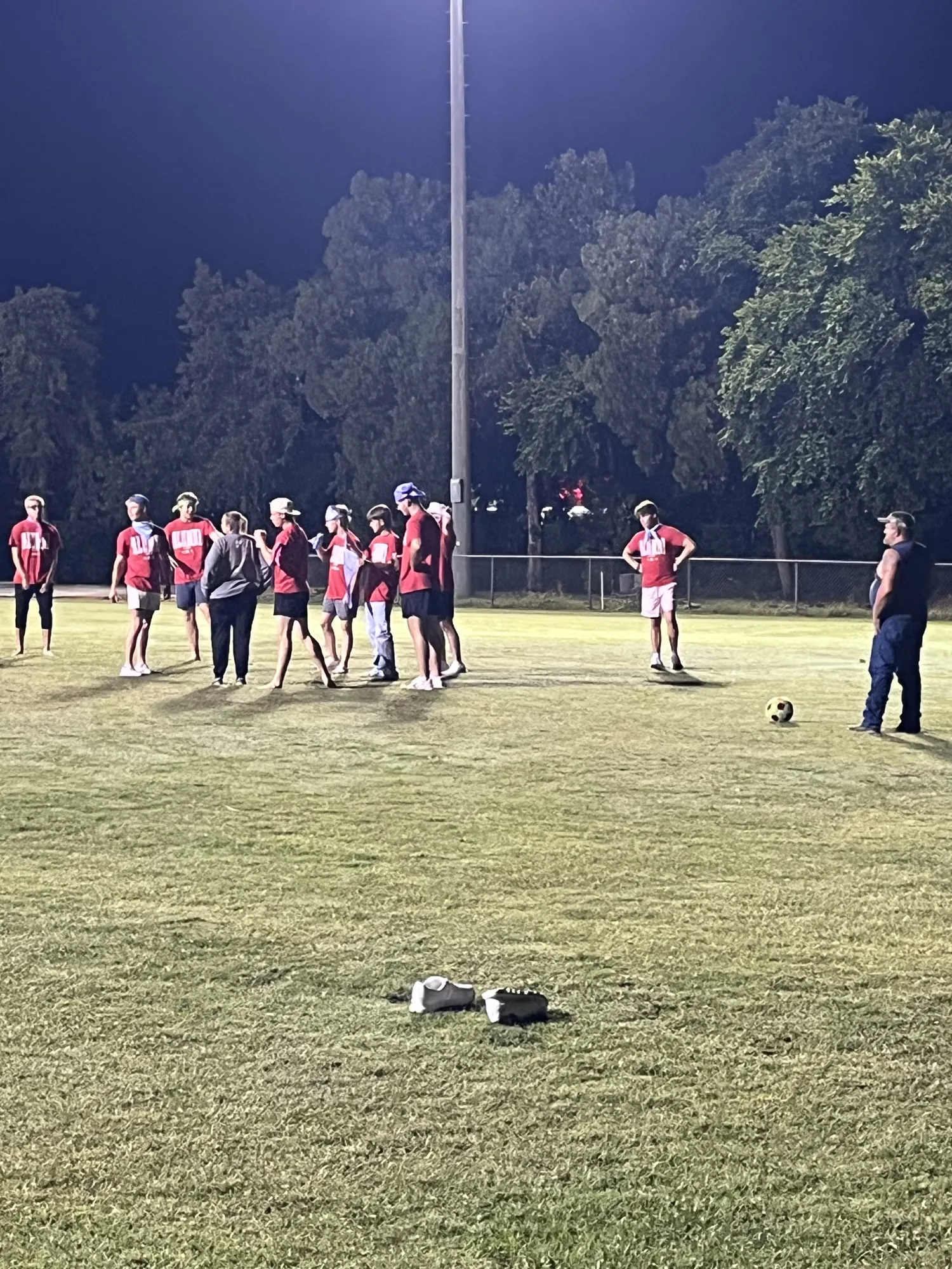 Seniors in matching red shirts on a lit-up football field during an all-night Project Graduation