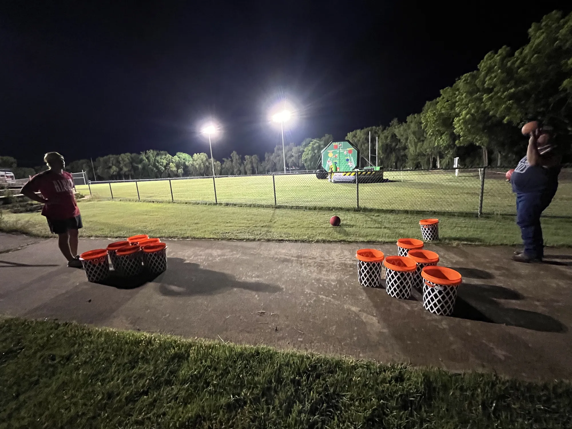 Basketball toss games set up on a path under stadium lights at a late-night Project Graduation party