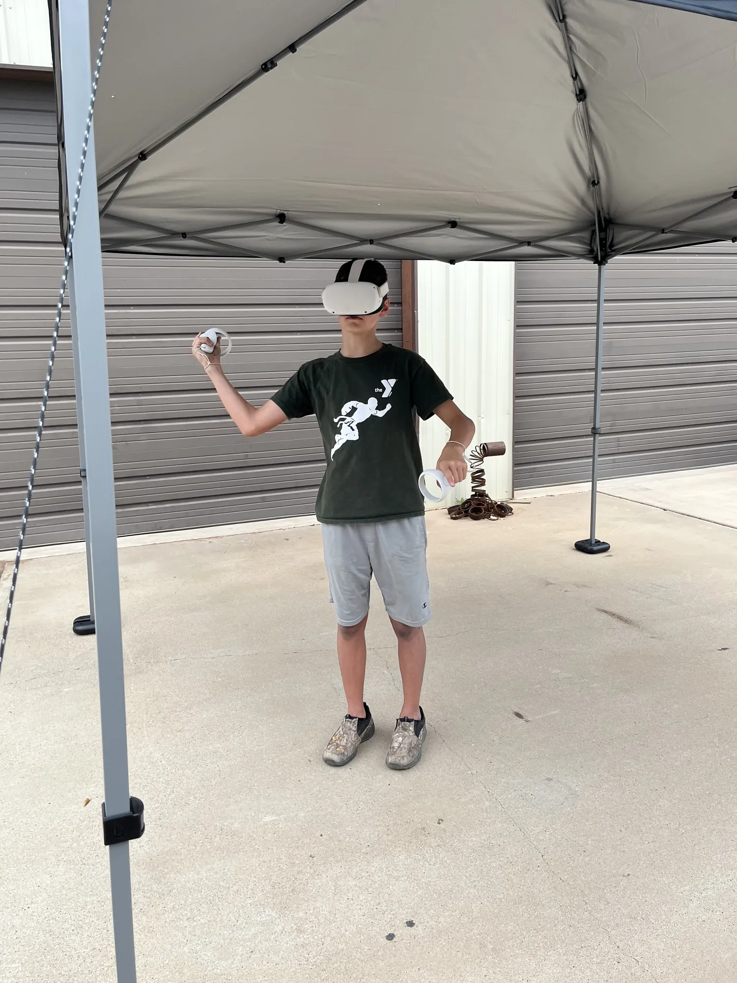 A boy in a VR headset swinging his controllers under our shade tent